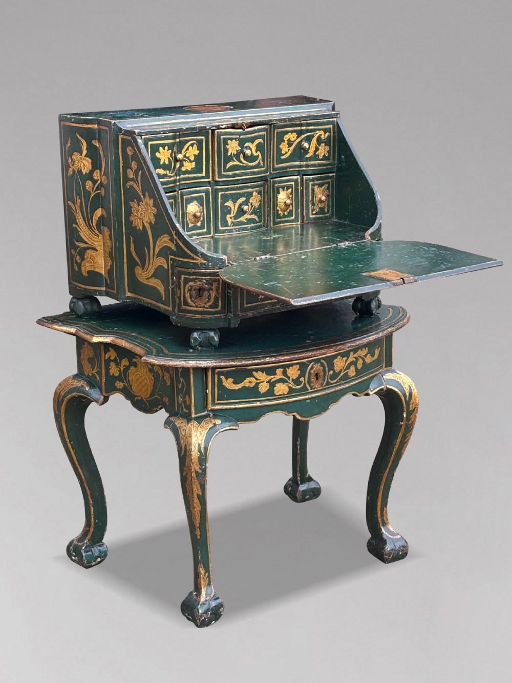An 18th-century Venetian dark green lacquered travelling bureau with gilded floral scrollwork and fall-front writing flap resting on a matching cabriole-leg stand.