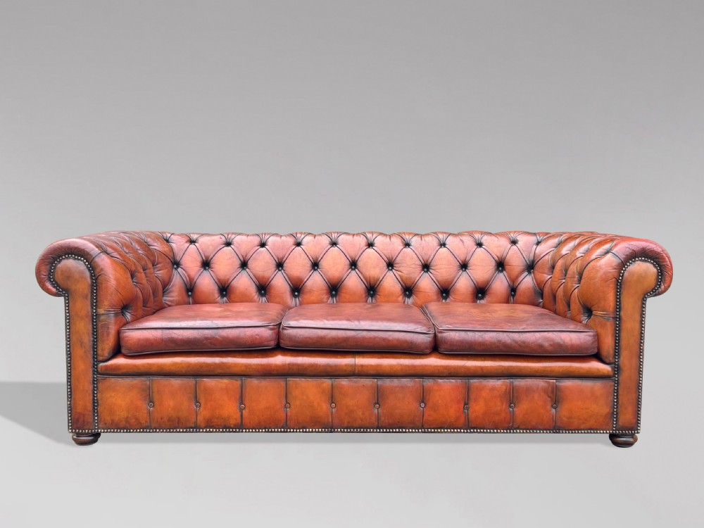 A three-seater brown leather Chesterfield sofa featuring deep button-tufted upholstery, rolled arms, brass studding, and three removable seat cushions.