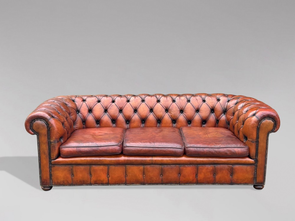 A three-seater brown leather Chesterfield sofa featuring deep button-tufted upholstery, rolled arms, brass studding, and three removable seat cushions. View II