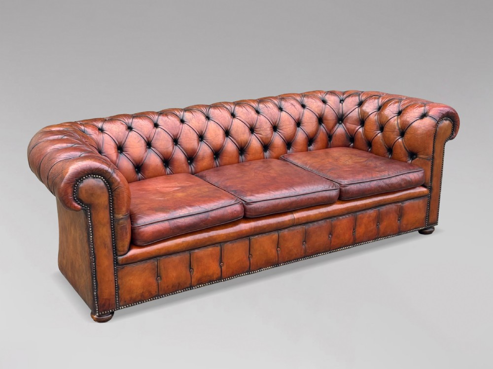 A three-seater brown leather Chesterfield sofa featuring deep button-tufted upholstery, rolled arms, brass studding, and three removable seat cushions. View III