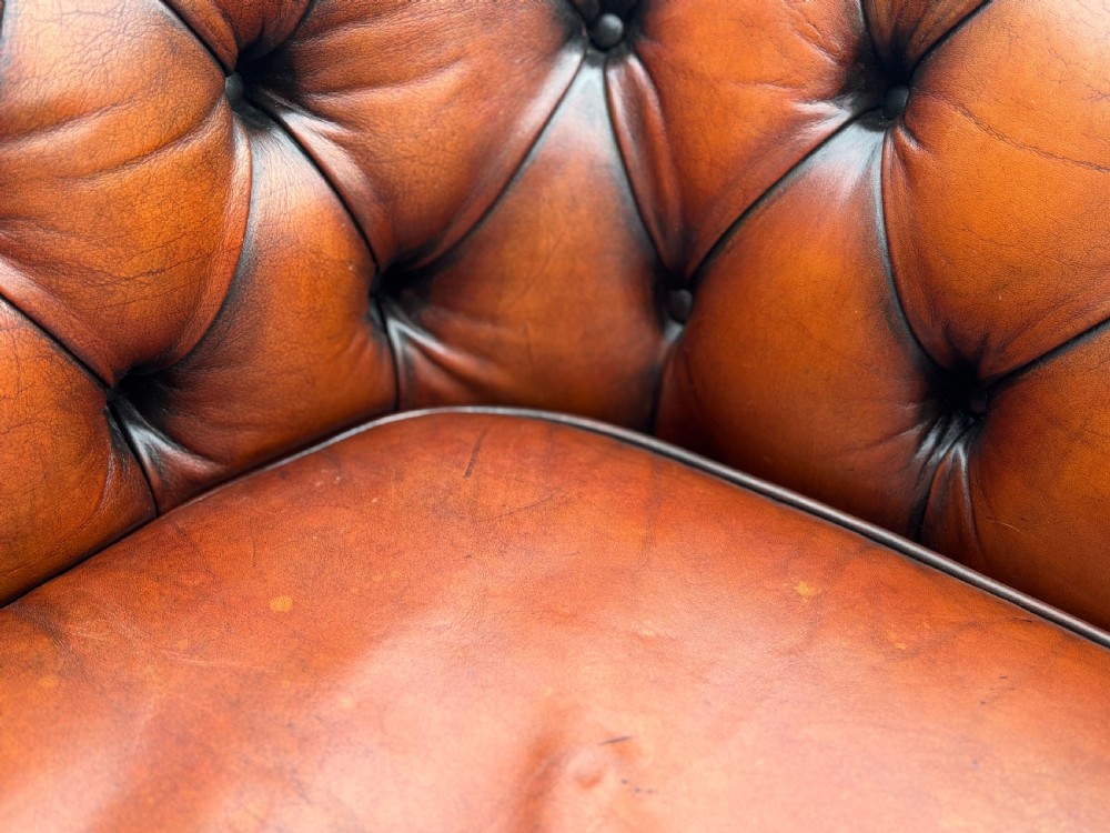A three-seater brown leather Chesterfield sofa featuring deep button-tufted upholstery, rolled arms, brass studding, and three removable seat cushions. View V