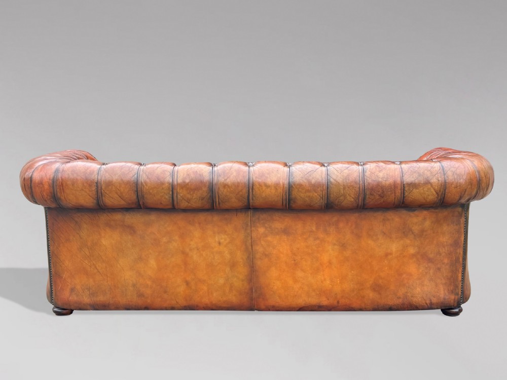 A three-seater brown leather Chesterfield sofa featuring deep button-tufted upholstery, rolled arms, brass studding, and three removable seat cushions. View VII