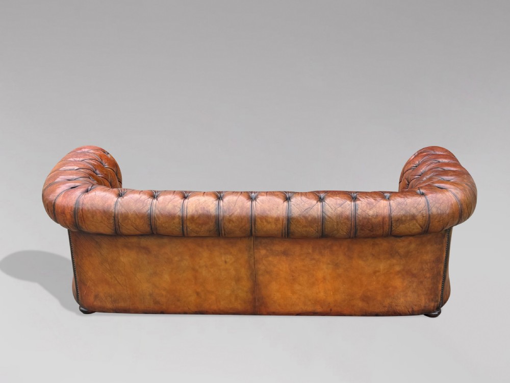 A three-seater brown leather Chesterfield sofa featuring deep button-tufted upholstery, rolled arms, brass studding, and three removable seat cushions. View VIII