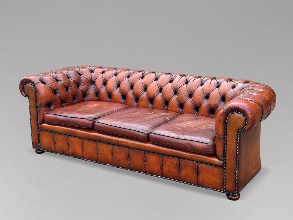 A three-seater brown leather Chesterfield sofa featuring deep button-tufted upholstery, rolled arms, brass studding, and three removable seat cushions. View X