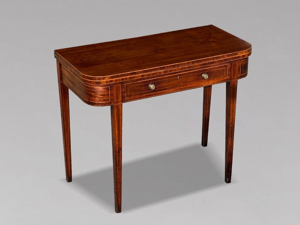 An 18th-century George III mahogany fold-over tea table featuring fine string inlay, a frieze drawer with brass handles, and tapered legs.
