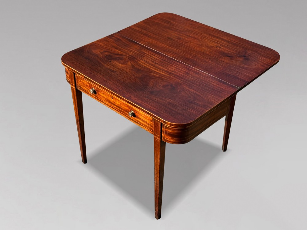 An 18th-century George III mahogany fold-over tea table featuring fine string inlay, a frieze drawer with brass handles, and tapered legs. View V