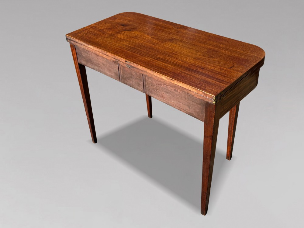 An 18th-century George III mahogany fold-over tea table featuring fine string inlay, a frieze drawer with brass handles, and tapered legs. View X