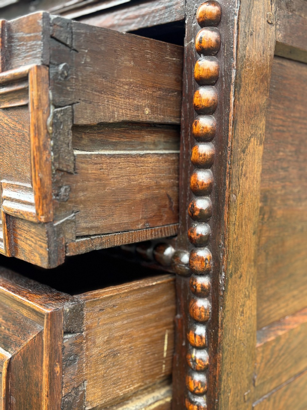 A 17th-century dark oak chest of drawers featuring three drawers decorated with raised geometric mitred mouldings, beaded trim details, and central brass drop handles. View VIII