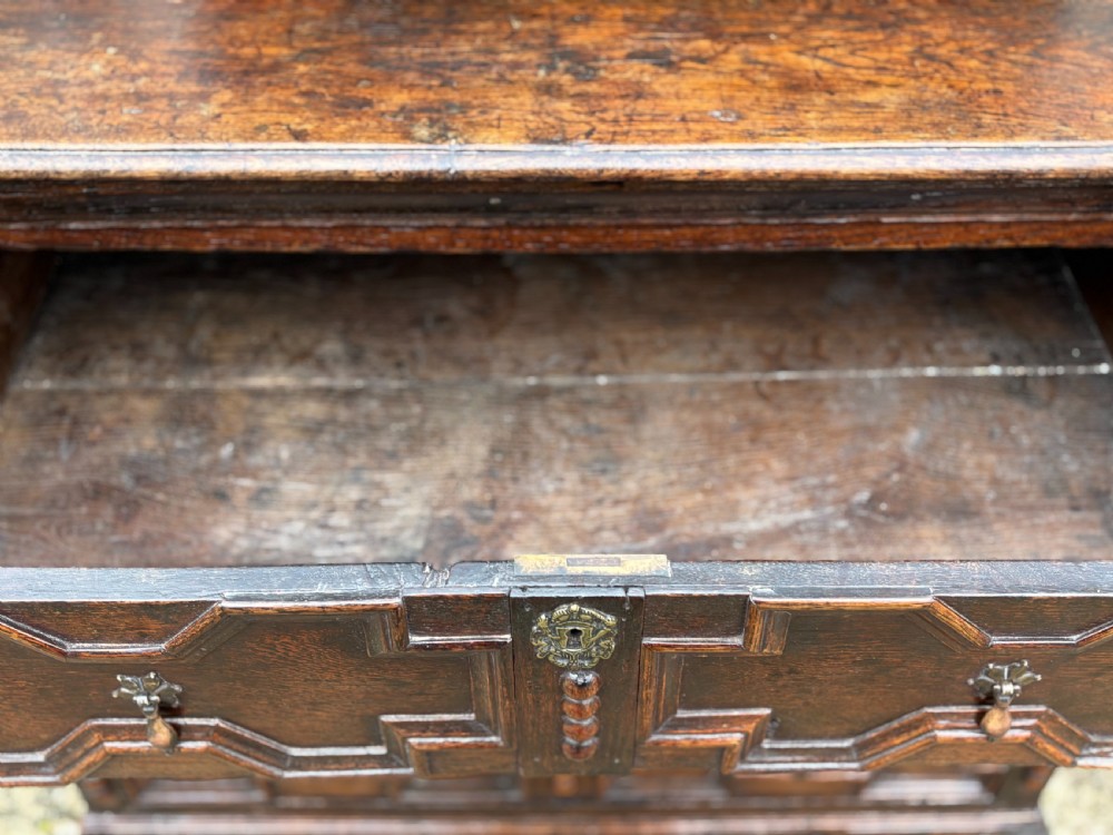 A 17th-century dark oak chest of drawers featuring three drawers decorated with raised geometric mitred mouldings, beaded trim details, and central brass drop handles. View X
