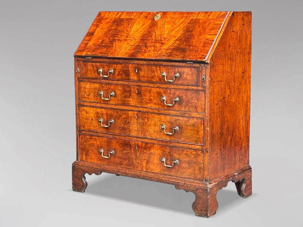 An 18th-century George III mahogany slant-front bureau featuring four graduated drawers with brass swan-neck handles and shaped bracket feet.