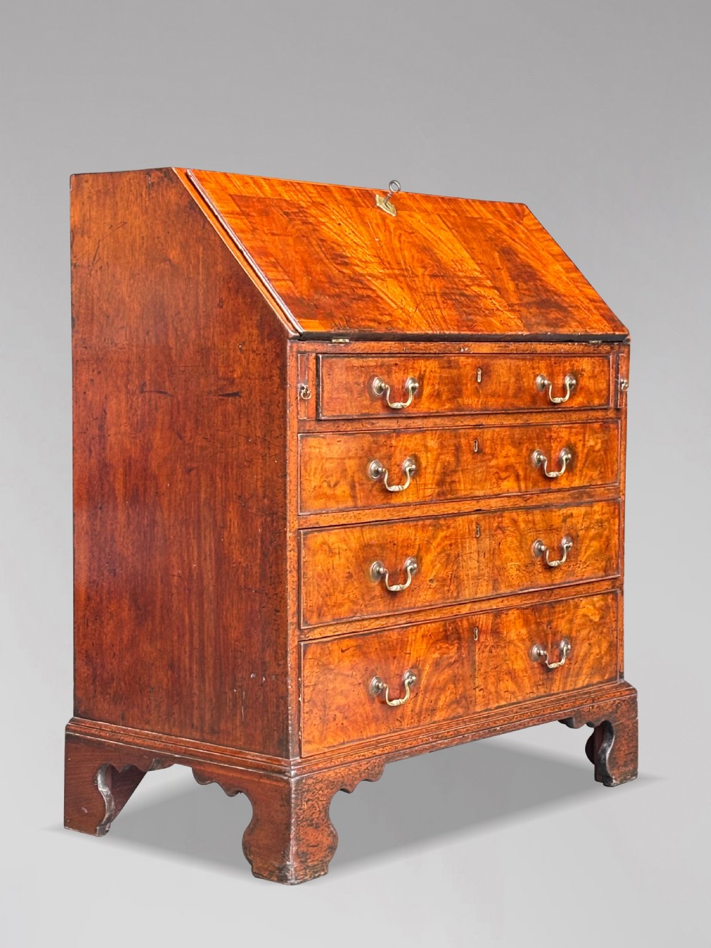 An 18th-century George III mahogany slant-front bureau featuring four graduated drawers with brass swan-neck handles and shaped bracket feet. View XI
