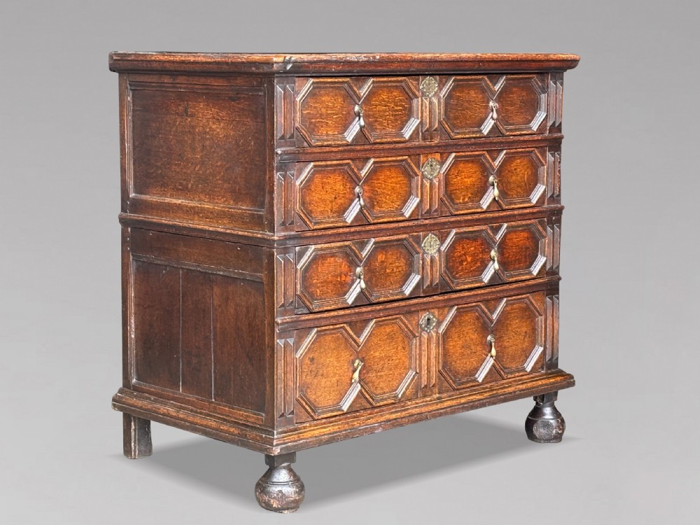 A seventeenth-century Charles II oak chest of drawers featuring four geometric panelled drawers with brass teardrop handles, resting on turned bun feet. View II