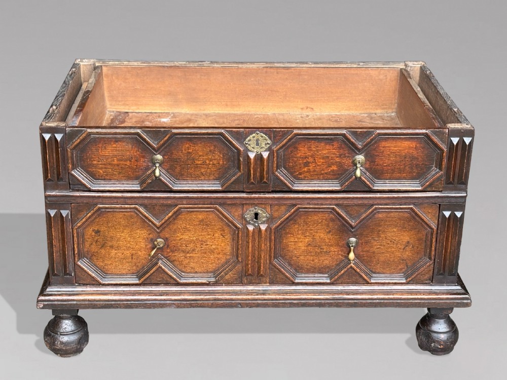A seventeenth-century Charles II oak chest of drawers featuring four geometric panelled drawers with brass teardrop handles, resting on turned bun feet. View III