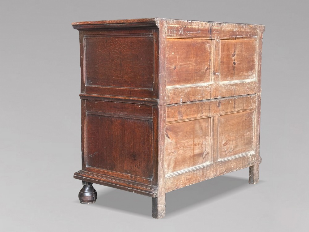A seventeenth-century Charles II oak chest of drawers featuring four geometric panelled drawers with brass teardrop handles, resting on turned bun feet. View V