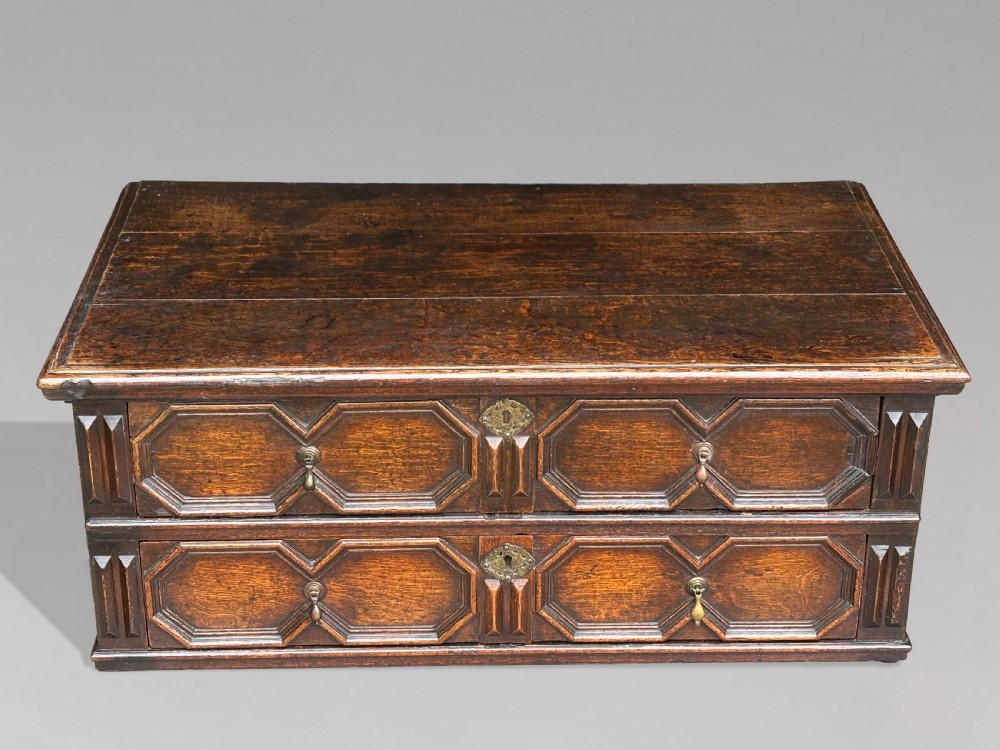 A seventeenth-century Charles II oak chest of drawers featuring four geometric panelled drawers with brass teardrop handles, resting on turned bun feet. View VI