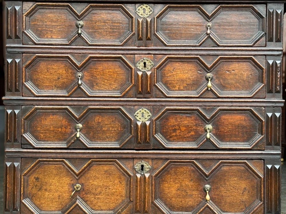 A seventeenth-century Charles II oak chest of drawers featuring four geometric panelled drawers with brass teardrop handles, resting on turned bun feet. View VII