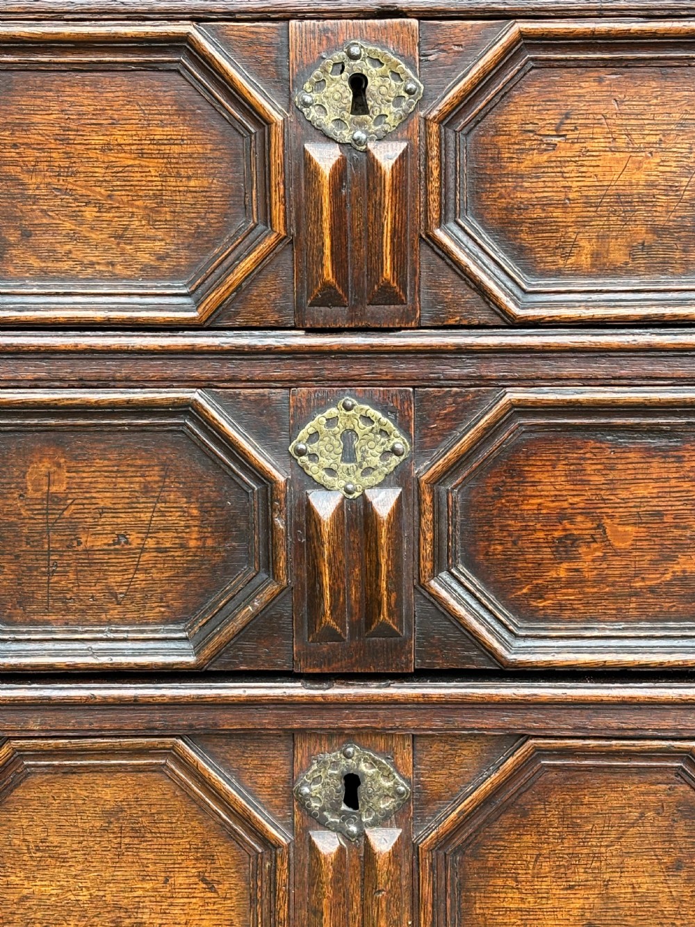 A seventeenth-century Charles II oak chest of drawers featuring four geometric panelled drawers with brass teardrop handles, resting on turned bun feet. View VIII