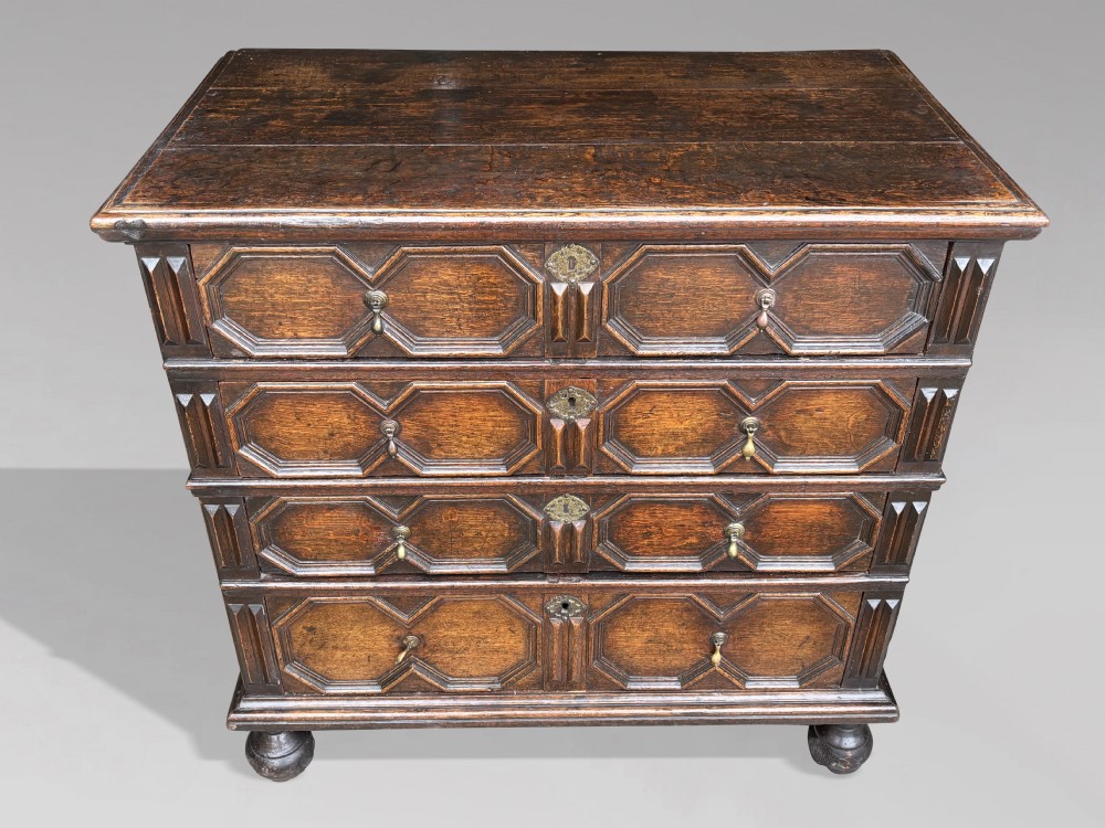 A seventeenth-century Charles II oak chest of drawers featuring four geometric panelled drawers with brass teardrop handles, resting on turned bun feet. View X