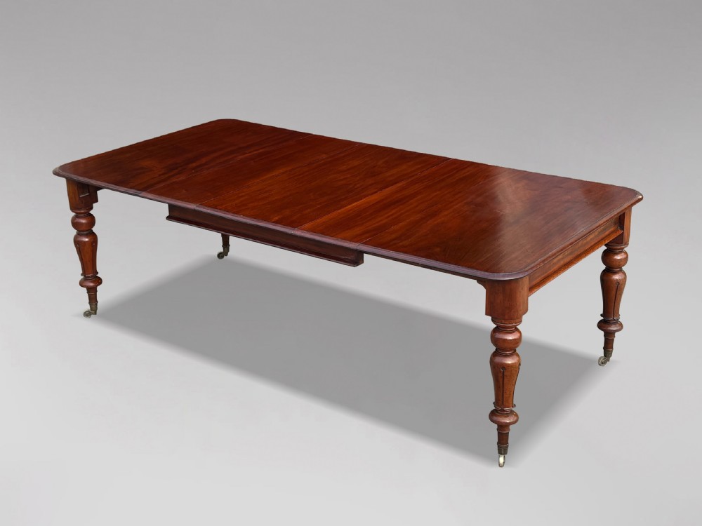 A 19th-century mahogany extending dining table featuring a polished rectangular top with rounded corners, supported by four heavy turned legs on brass castors.