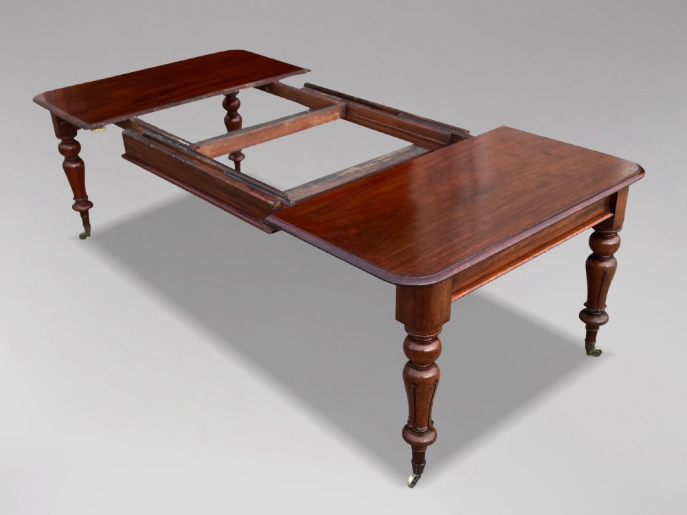 A 19th-century mahogany extending dining table featuring a polished rectangular top with rounded corners, supported by four heavy turned legs on brass castors. View II