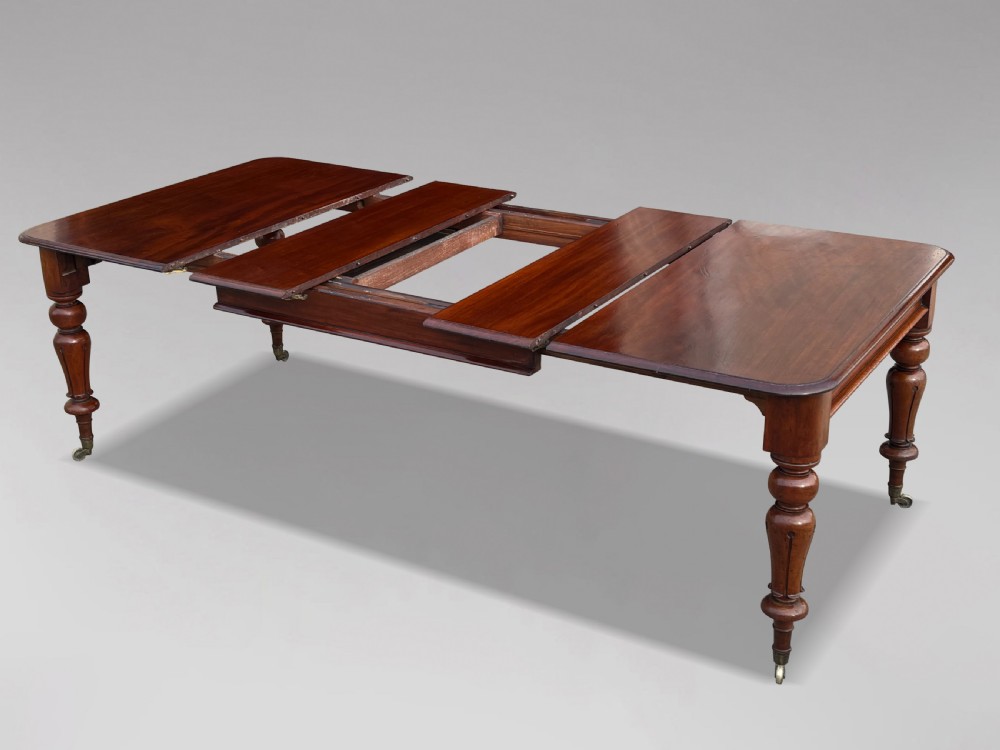 A 19th-century mahogany extending dining table featuring a polished rectangular top with rounded corners, supported by four heavy turned legs on brass castors. View III