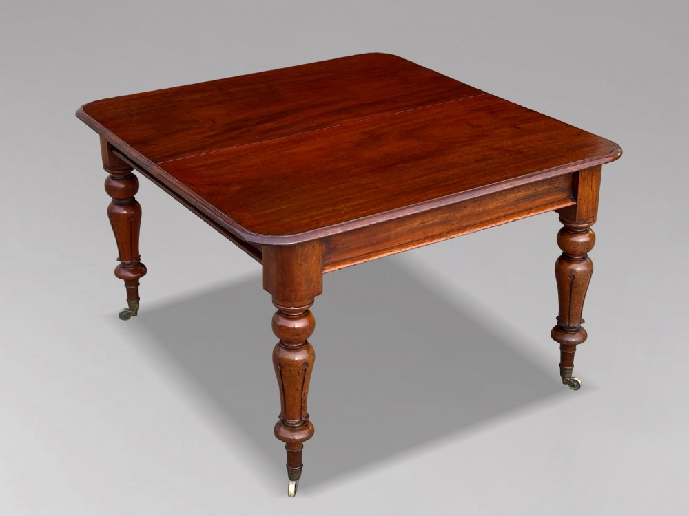 A 19th-century mahogany extending dining table featuring a polished rectangular top with rounded corners, supported by four heavy turned legs on brass castors. View V