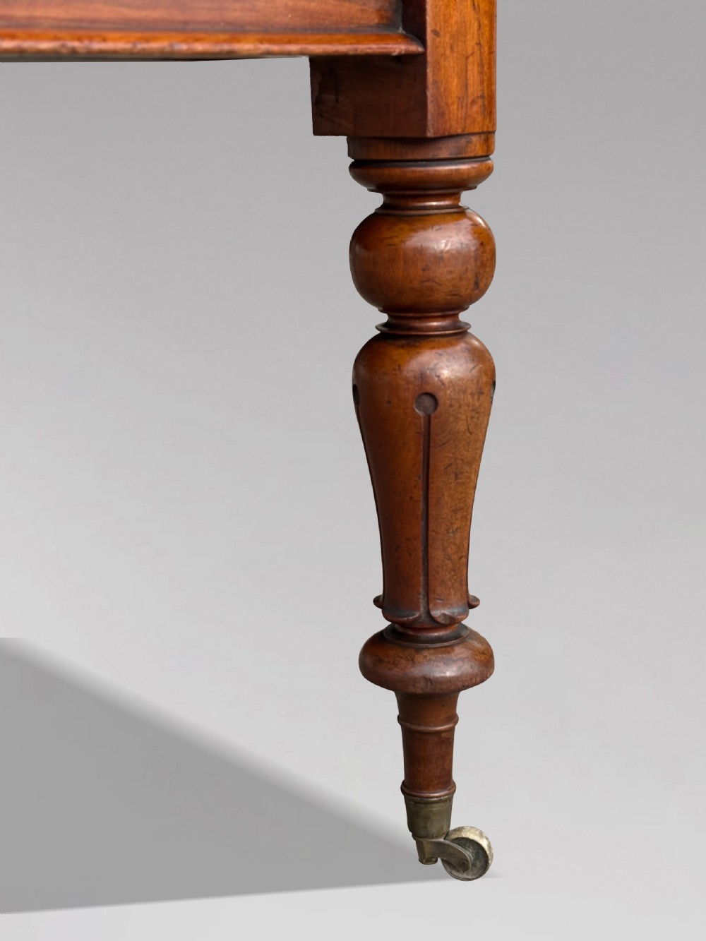 A 19th-century mahogany extending dining table featuring a polished rectangular top with rounded corners, supported by four heavy turned legs on brass castors. View VI