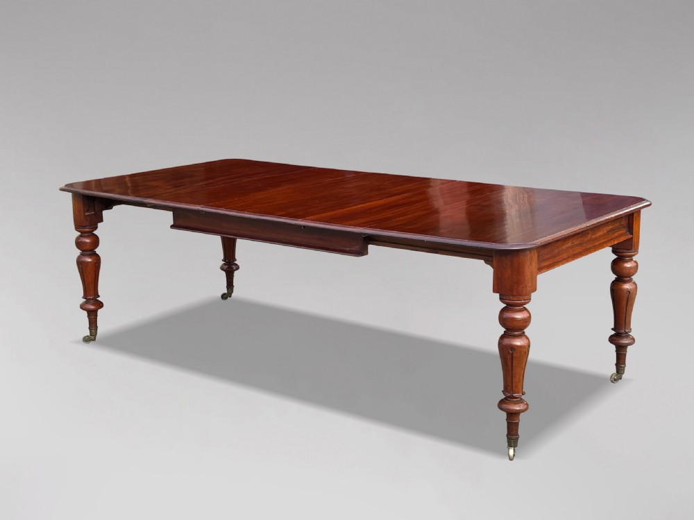 A 19th-century mahogany extending dining table featuring a polished rectangular top with rounded corners, supported by four heavy turned legs on brass castors. View VIII