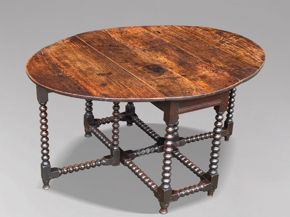 A 17th-century Charles II dark oak gateleg table featuring an oval drop-leaf top supported by bobbin-turned legs and stretchers.