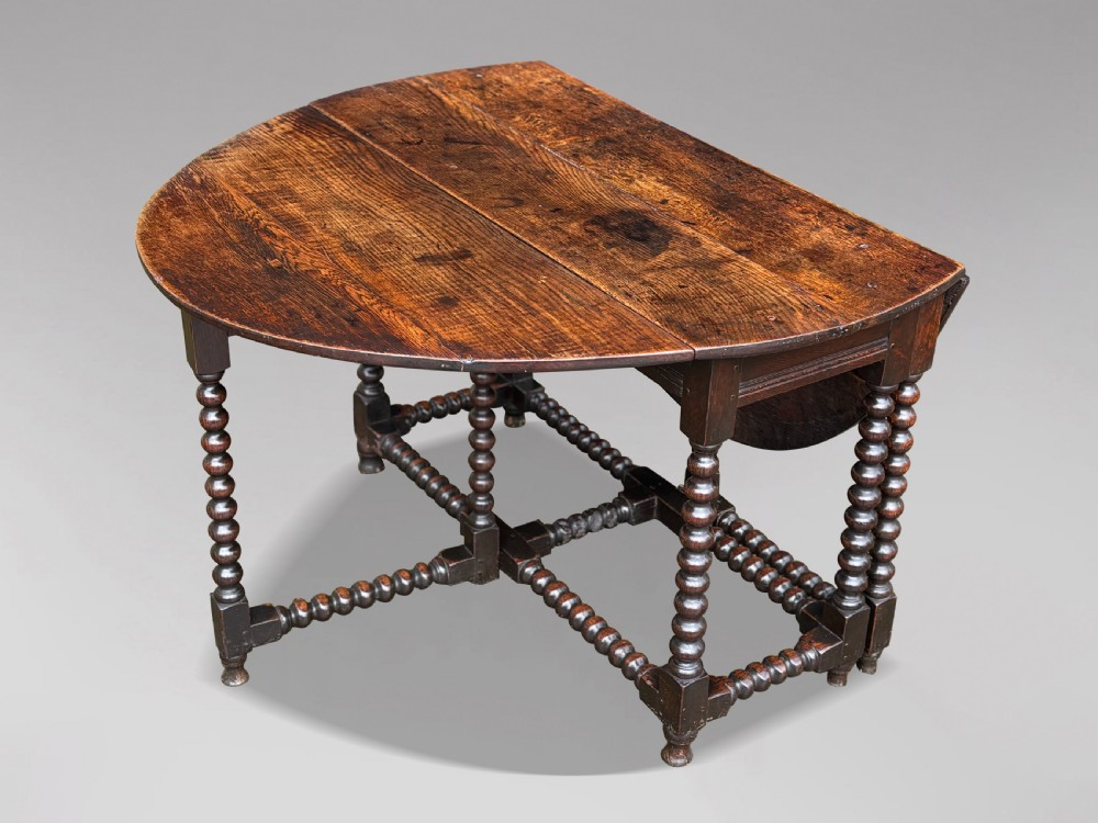 A 17th-century Charles II dark oak gateleg table featuring an oval drop-leaf top supported by bobbin-turned legs and stretchers. View IV
