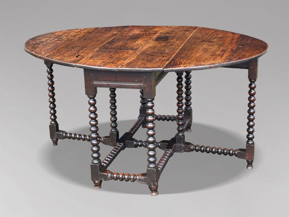 A 17th-century Charles II dark oak gateleg table featuring an oval drop-leaf top supported by bobbin-turned legs and stretchers. View VI