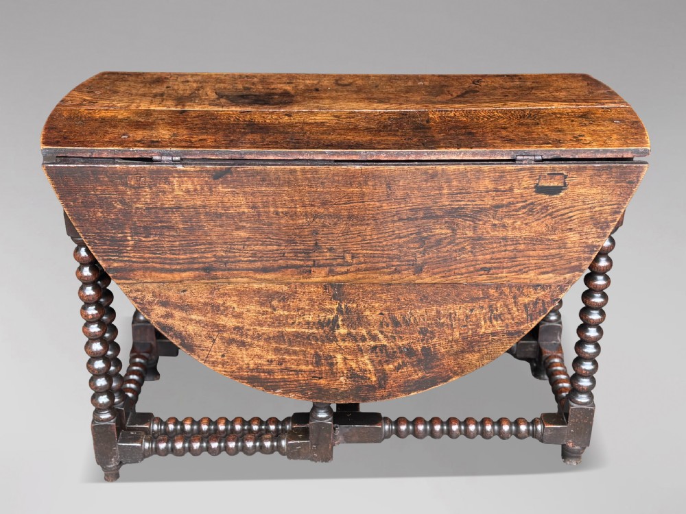 A 17th-century Charles II dark oak gateleg table featuring an oval drop-leaf top supported by bobbin-turned legs and stretchers. View VII
