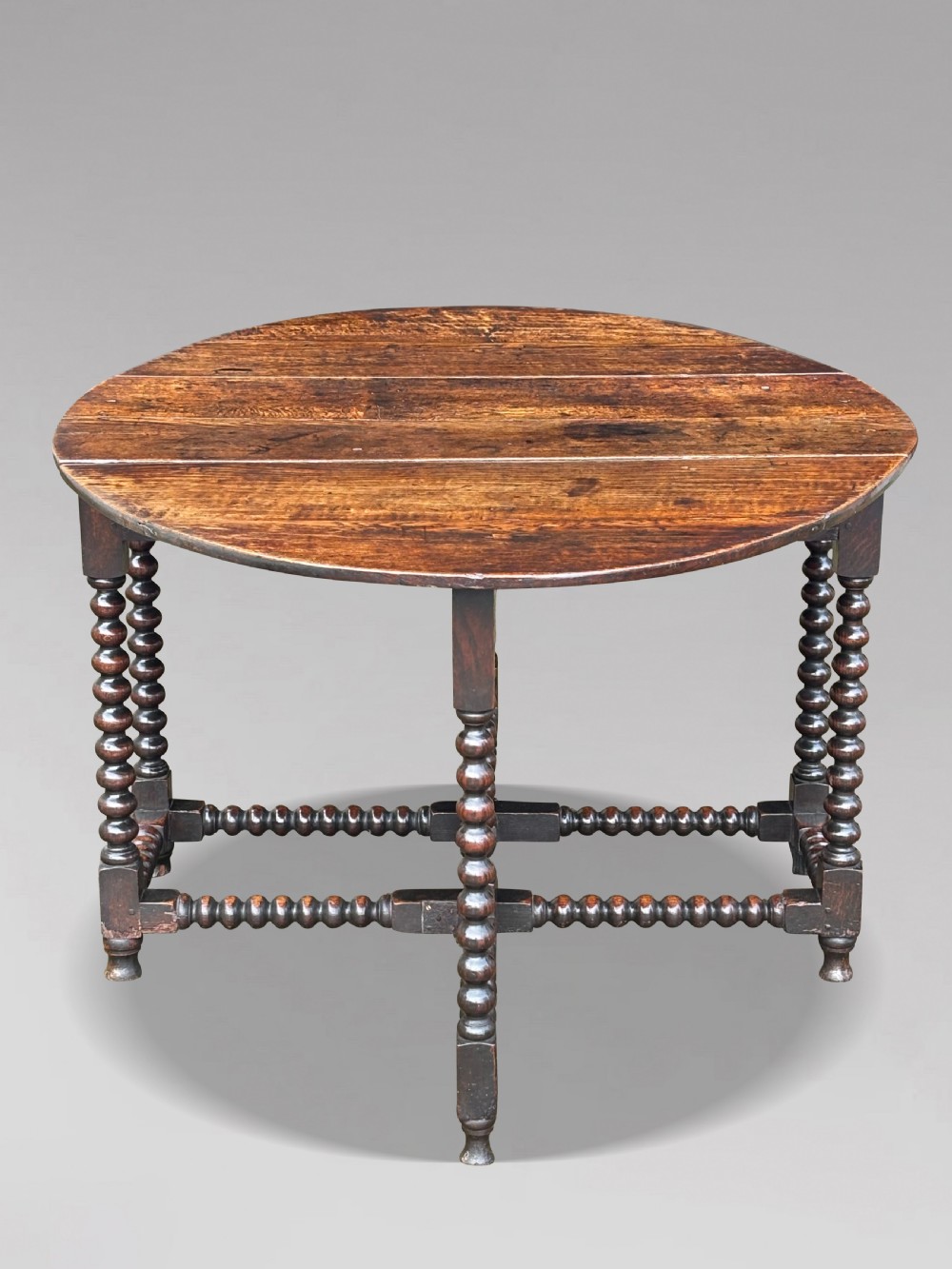 A 17th-century Charles II dark oak gateleg table featuring an oval drop-leaf top supported by bobbin-turned legs and stretchers. View VIII