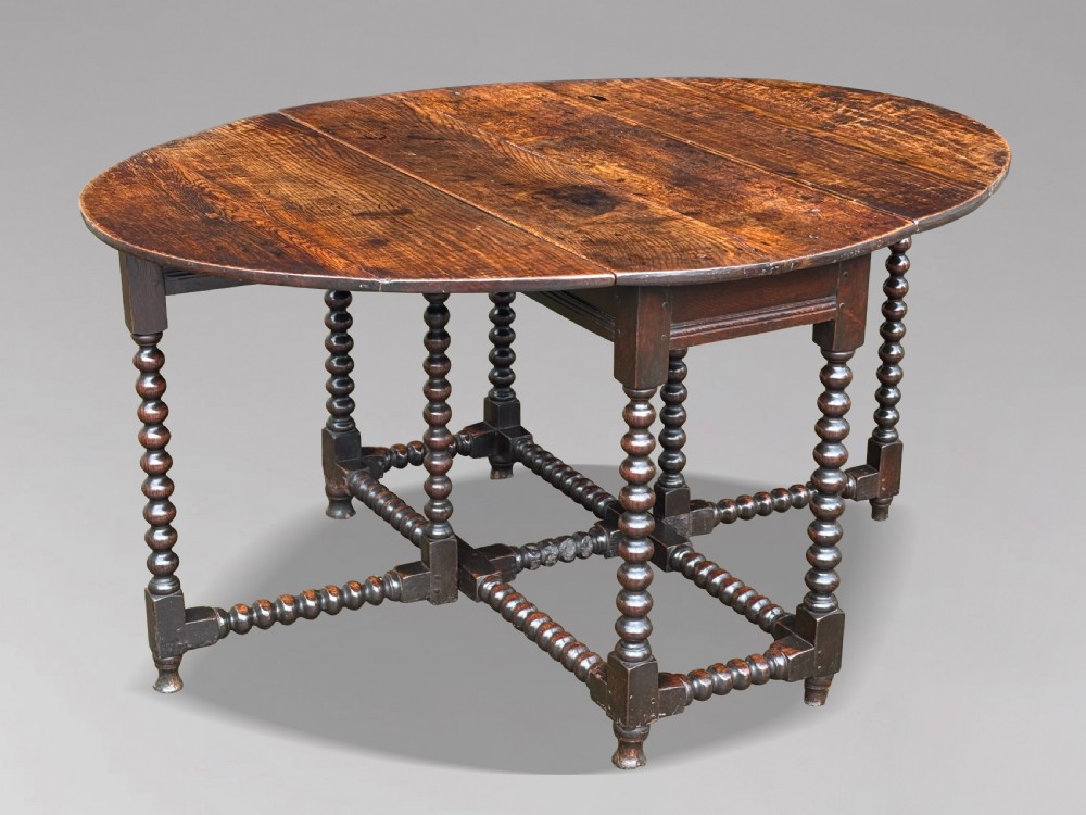 A 17th-century Charles II dark oak gateleg table featuring an oval drop-leaf top supported by bobbin-turned legs and stretchers. View IX