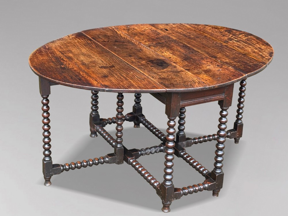 A 17th-century Charles II dark oak gateleg table featuring an oval drop-leaf top supported by bobbin-turned legs and stretchers. View X