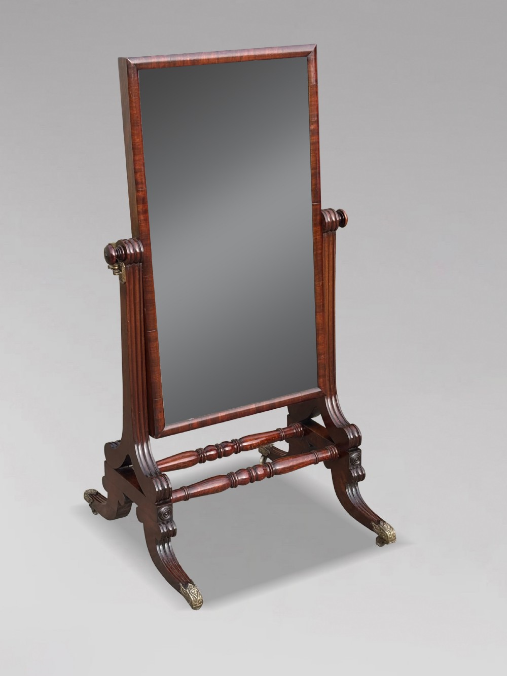 A 19th-century William IV mahogany cheval mirror featuring a rectangular swivel glass plate, dual brass candle sconces, turned stretchers, and splayed legs with brass claw feet on castors. View II