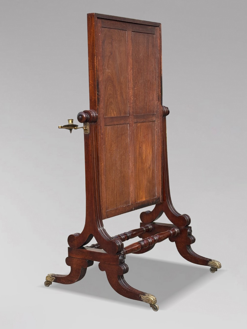 A 19th-century William IV mahogany cheval mirror featuring a rectangular swivel glass plate, dual brass candle sconces, turned stretchers, and splayed legs with brass claw feet on castors. View III
