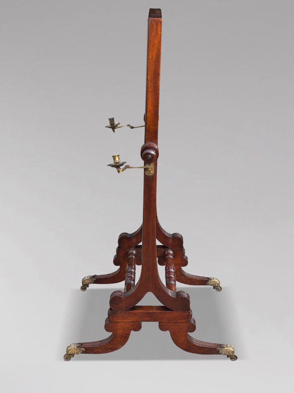 A 19th-century William IV mahogany cheval mirror featuring a rectangular swivel glass plate, dual brass candle sconces, turned stretchers, and splayed legs with brass claw feet on castors. View VI