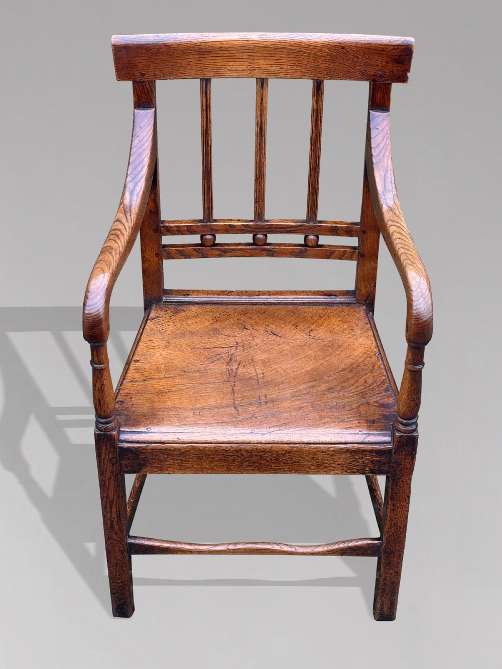 An 18th-century George III elm country armchair featuring a solid timber seat, curved arms, vertical back splats, and square legs.