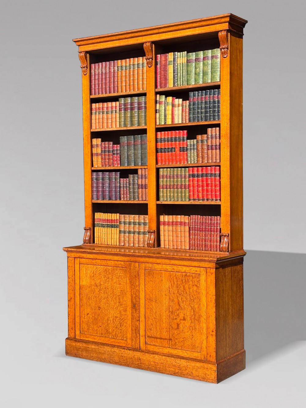 A two-section 19th-century oak open bookcase featuring carved corbels flanking the upper shelves and a double-panelled cupboard base. View II