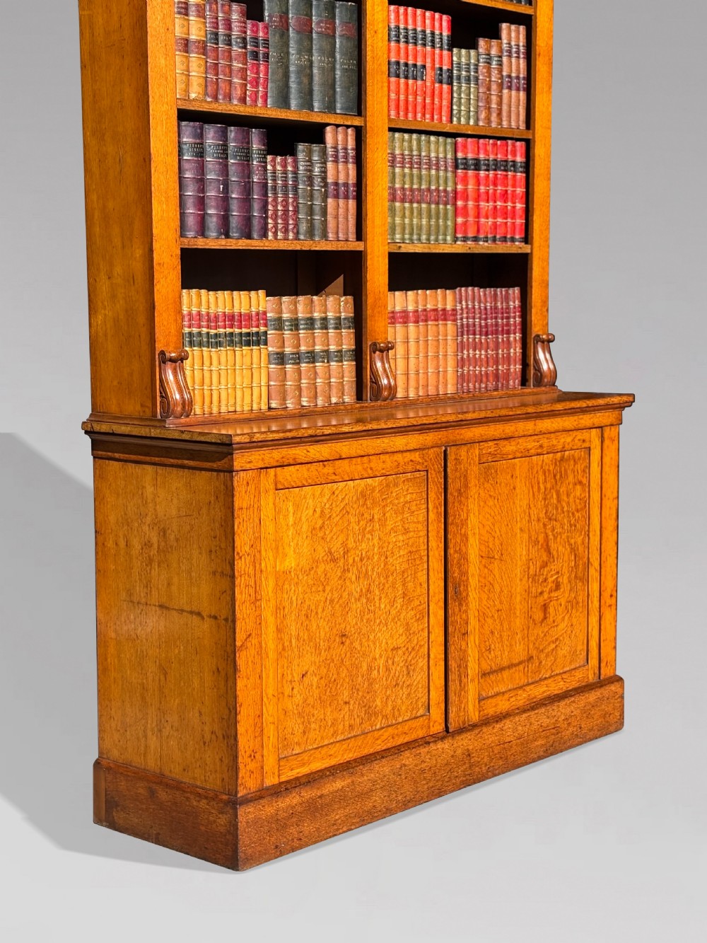 A two-section 19th-century oak open bookcase featuring carved corbels flanking the upper shelves and a double-panelled cupboard base. View IV