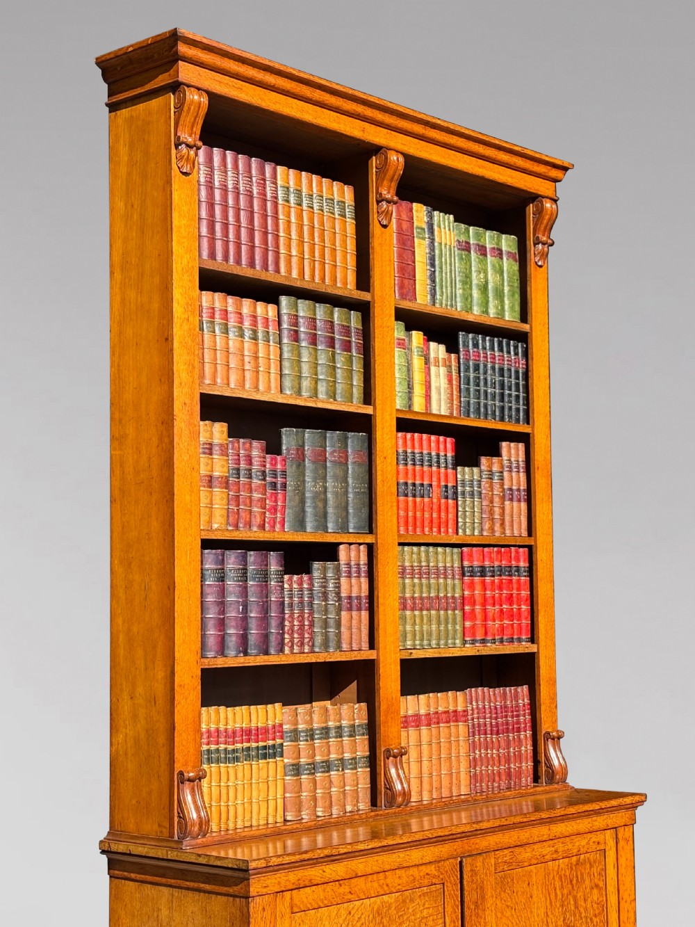 A two-section 19th-century oak open bookcase featuring carved corbels flanking the upper shelves and a double-panelled cupboard base. View V
