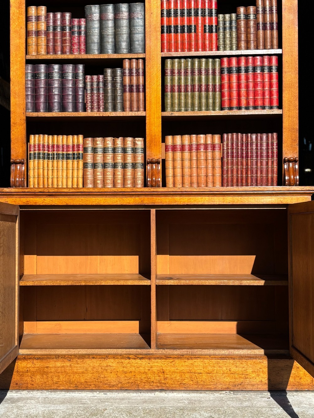 A two-section 19th-century oak open bookcase featuring carved corbels flanking the upper shelves and a double-panelled cupboard base. View VI