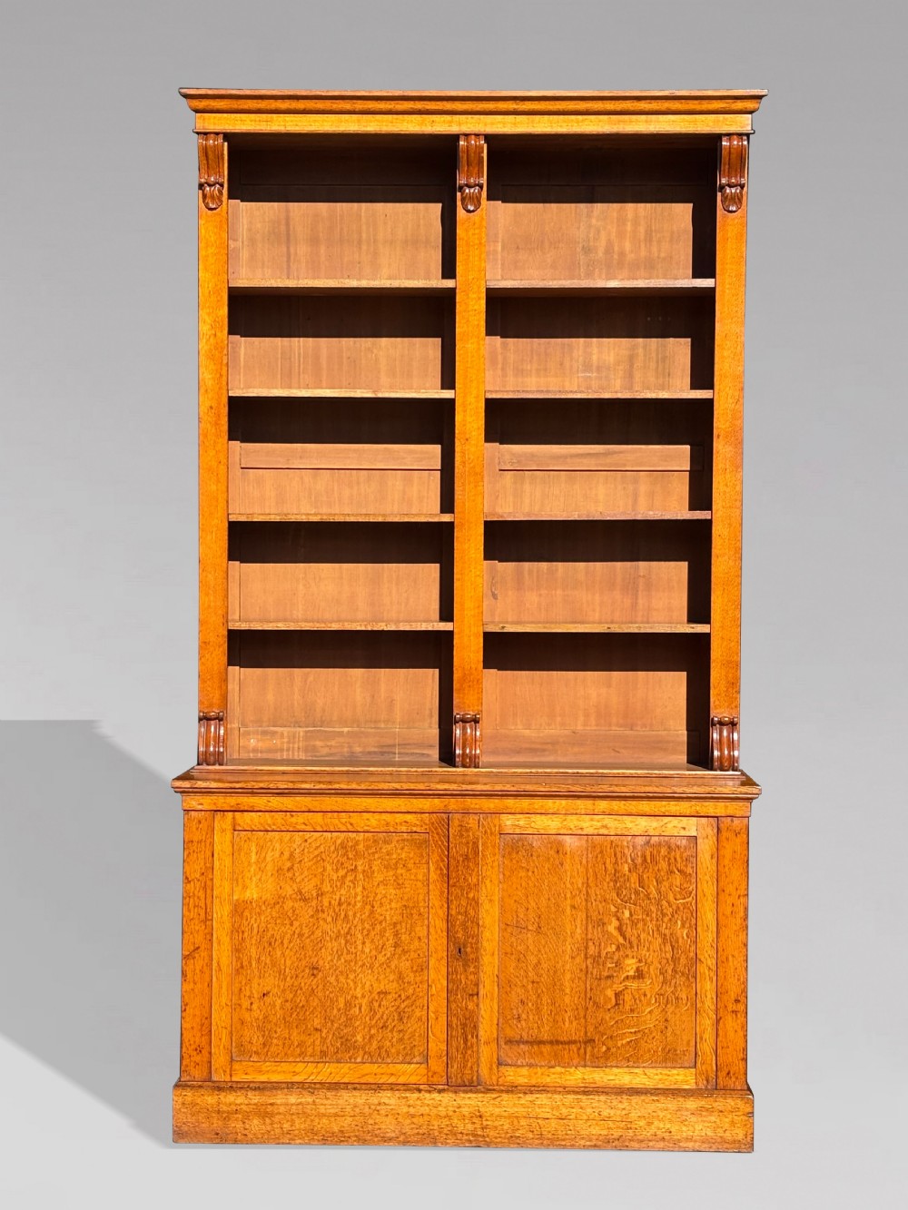 A two-section 19th-century oak open bookcase featuring carved corbels flanking the upper shelves and a double-panelled cupboard base. View VII