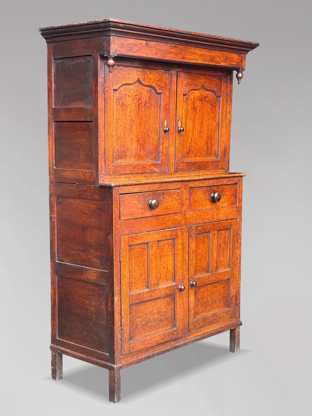 An eighteenth-century George III oak court cupboard featuring an overhanging canopy with turned pendants, upper panelled doors, two drawers, and a double-door base.