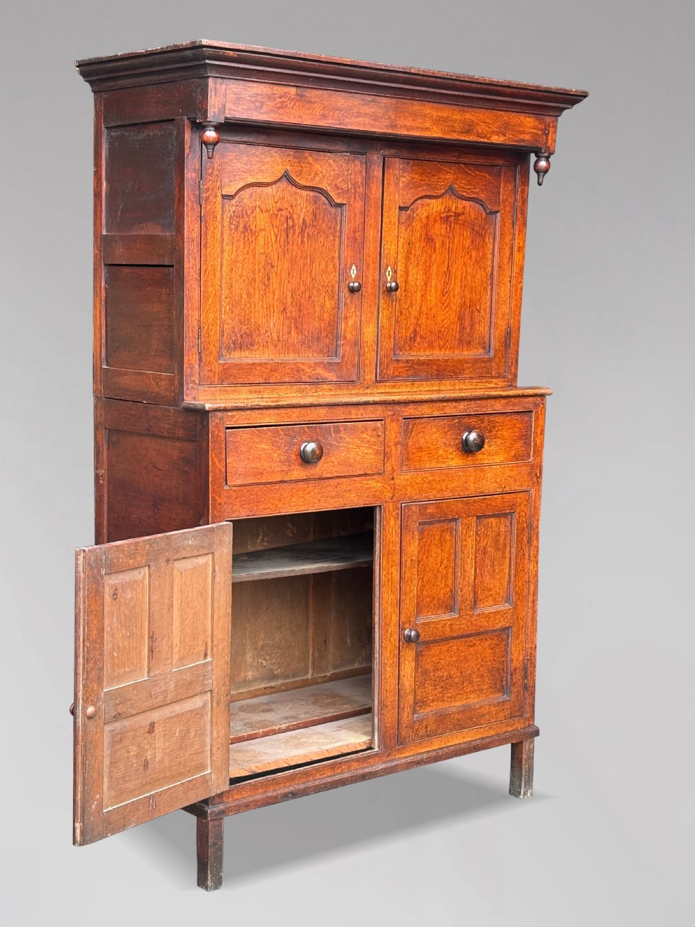 An eighteenth-century George III oak court cupboard featuring an overhanging canopy with turned pendants, upper panelled doors, two drawers, and a double-door base. View XI