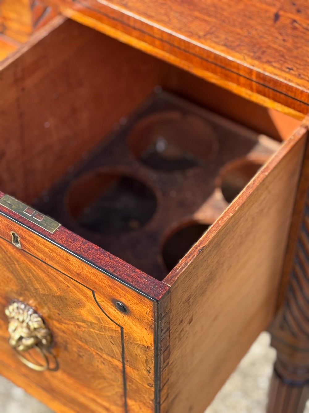 A 19th-century George IV flame mahogany breakfront sideboard featuring ebony stringing, lion-mask brass handles, spiral pilasters, and fluted legs. View VII