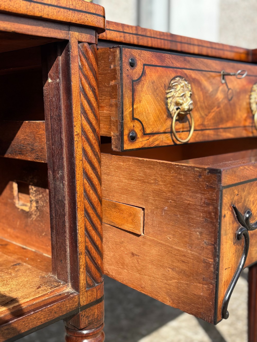A 19th-century George IV flame mahogany breakfront sideboard featuring ebony stringing, lion-mask brass handles, spiral pilasters, and fluted legs. View VIII