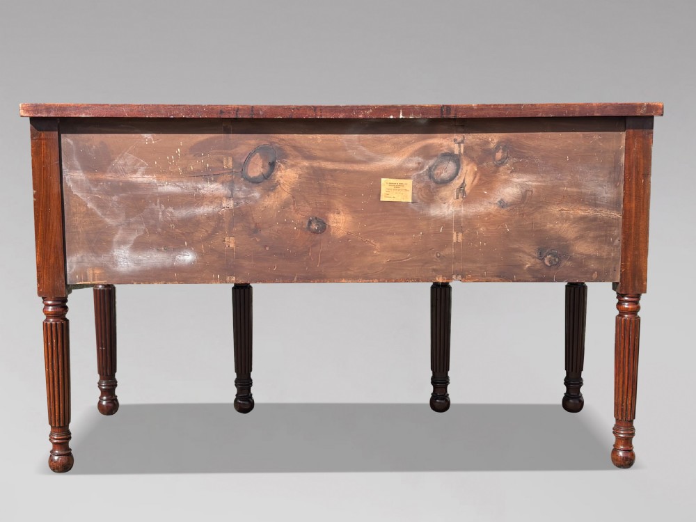 A 19th-century George IV flame mahogany breakfront sideboard featuring ebony stringing, lion-mask brass handles, spiral pilasters, and fluted legs. View X