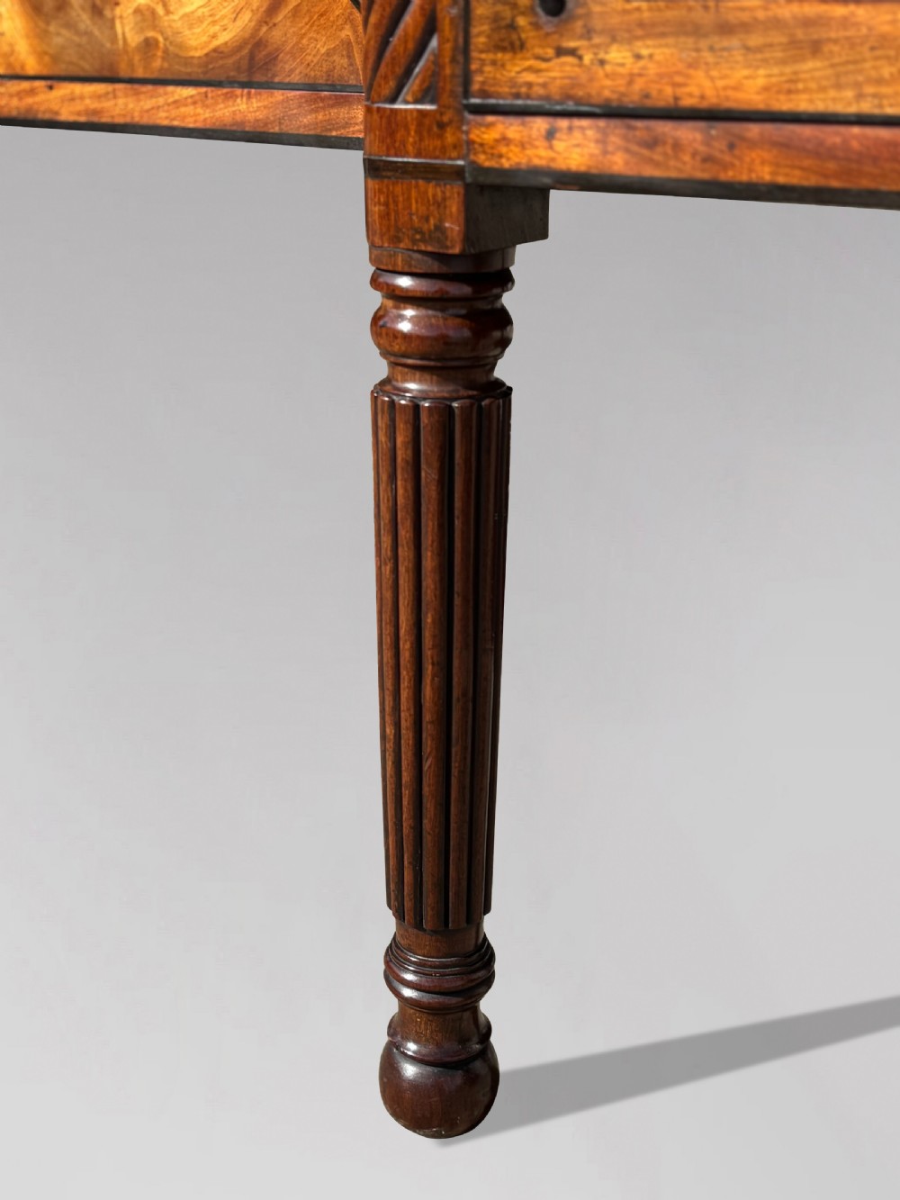 A 19th-century George IV flame mahogany breakfront sideboard featuring ebony stringing, lion-mask brass handles, spiral pilasters, and fluted legs. View XI